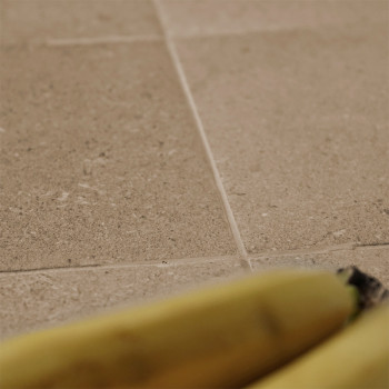 Uma banana repousa sobre ladrilhos de pedra, apresentando superfície texturizada e tons neutros, criando um ambiente natural e t