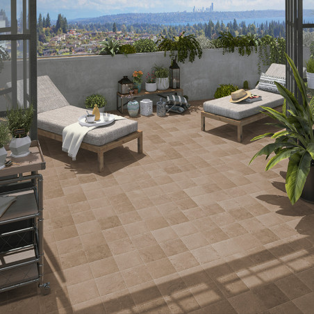 Deux chaises longues avec coussins et tables d'appoint sont installées sur une terrasse carrelée. Entourée de plantes en pot, la