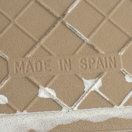 O ladrilho cerâmico bege apresenta o texto em relevo `MADE IN SPAIN,` exibindo um padrão de diamante com manchas brancas irregul