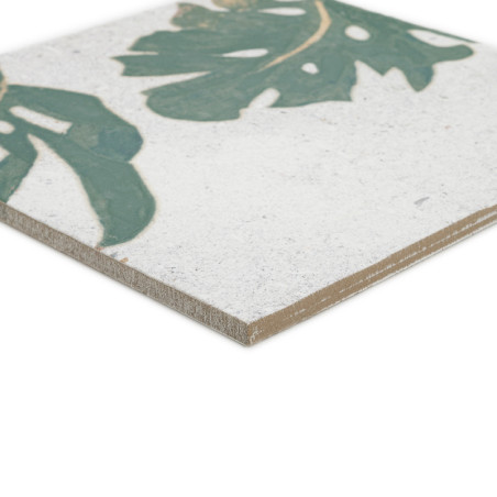 Un azulejo cerámico muestra un motivo de hoja verde sobre un fondo blanco. Su borde está ligeramente biselado, destacando el esp
