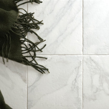 Un tissu à franges sombre recouvre quatre carreaux clairs à motifs de marbre, créant un contraste de texture et de couleur dans 