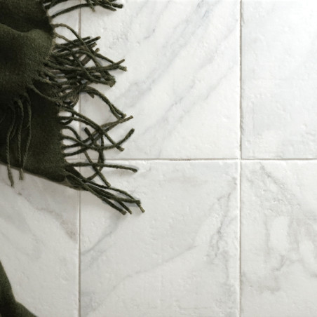 Un tissu à franges sombre recouvre quatre carreaux clairs à motifs de marbre, créant un contraste de texture et de couleur dans 