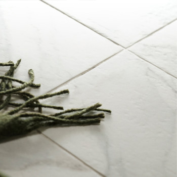 Des carreaux de marbre blanc reposent à plat sur le sol, avec des franges vertes provenant d'un tapis voisin les recouvrant part