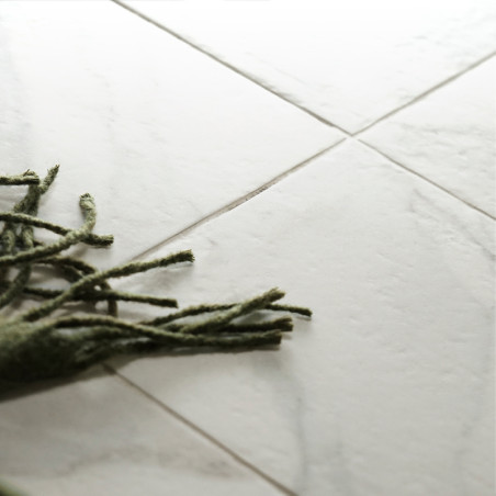 Des carreaux de marbre blanc reposent à plat sur le sol, avec des franges vertes provenant d'un tapis voisin les recouvrant part