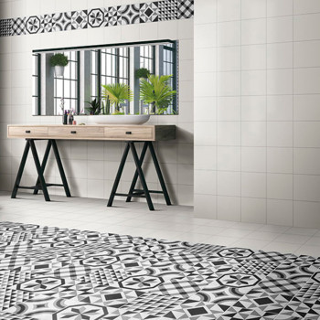 Un bureau en bois aux pieds noirs se dresse devant un miroir reflétant des plantes en pot. Des carreaux à motifs géométriques re