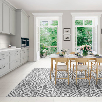Een eettafel met houten stoelen staat op een grijze en witte tegelvloer met een patroon, omgeven door witte keukenkasten en grot