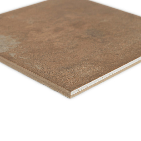 Um ladrilho cerâmico quadrado marrom com texturas sutis repousa sobre um fundo branco, revelando sua borda em camadas e superfíc