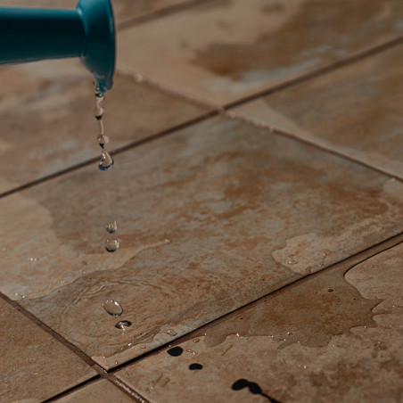 Water druppelt uit een blauwe tuit op bruine, getextureerde tegels, waardoor kleine plassen en een nat oppervlak ontstaan ​​in e