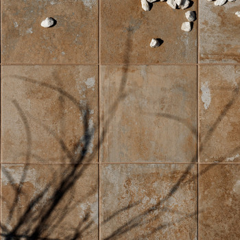 Bruine, getextureerde tegels vormen een raster. verspreide witte steentjes rusten op het oppervlak, terwijl schaduwen van boomta