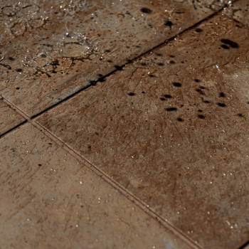 Bruine vierkante tegels vertonen waterdruppels en donkere vlekken, wat duidt op recente lekkage of regenval. De scène wordt verl