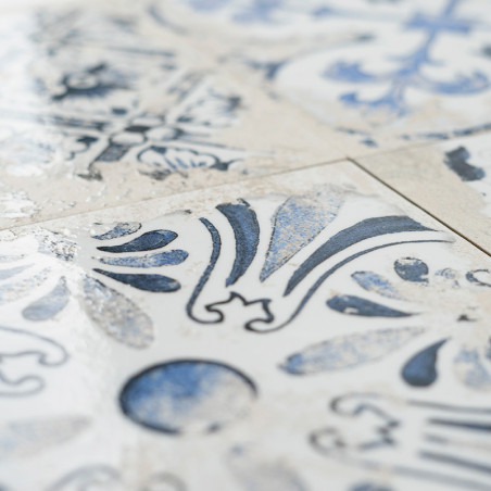 Un carreau de céramique présente des motifs floraux et géométriques bleus complexes, disposés symétriquement, sur un fond blanc,