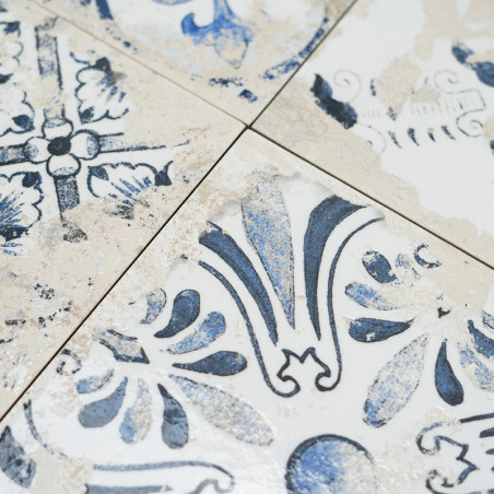 Les carreaux affichent des motifs floraux bleus complexes avec un aspect patiné. Ils se croisent aux lignes épurées, créant une 
