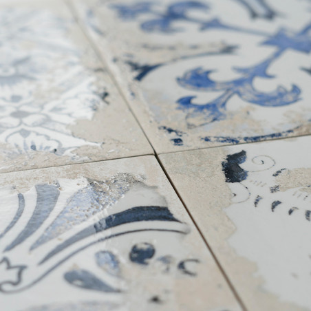 Quatre carreaux de céramique présentent des motifs floraux bleus et blancs à l'aspect patiné. Le gros plan montre des fissures e