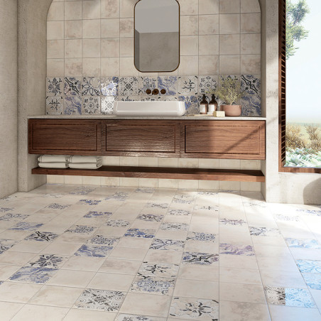 Une salle de bains présente des carreaux à motifs floraux recouvrant le sol et une partie du mur. Une vanité en bois contient un