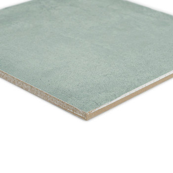 A square, green ceramic tile rests on a white surface, showcasing a smooth texture and slightly beveled edges, ideal for indoor 