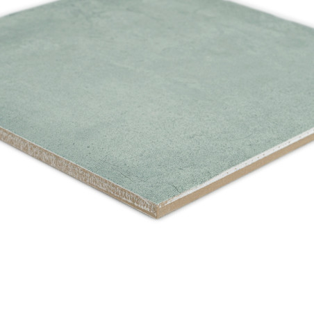 Un carreau de céramique carré vert repose sur une surface blanche, présentant une texture lisse et des bords légèrement biseauté