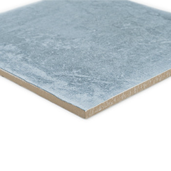 Carreau carré en céramique avec une surface bleu clair texturée, reposant à plat. Le bord révèle une couche brun clair.