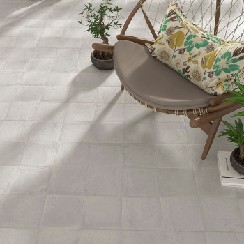 Um piso de mosaico bege é colocado horizontalmente, adjacente a uma moderna cadeira redonda com almofada floral, cercada por vas