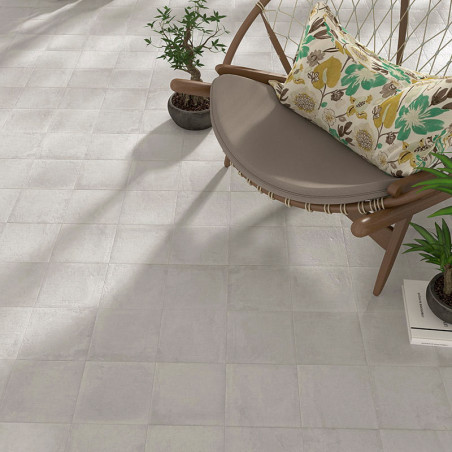 Horizontaal is een beige mozaïektegelvloer gelegd, grenzend aan een moderne, ronde stoel met bloemenkussen, omgeven door potplan Horizontaal is een beige mozaïektegelvloer gelegd, grenzend aan een moderne, ronde stoel met bloemenkussen, omgeven door potplan