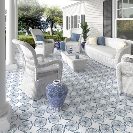 Weiße Korbmöbel stehen auf einer gemusterten blau-weiß gefliesten Terrasse. Umliegende Pflanzen und Bäume schmücken den großzügi