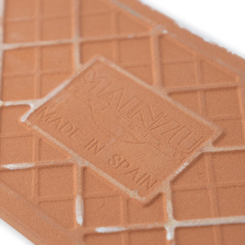 Azulejos de terracota con texto `MAUNZU` y `MADE IN SPAIN`. El azulejo presenta un patrón de cuadrícula geométrico con un ligero