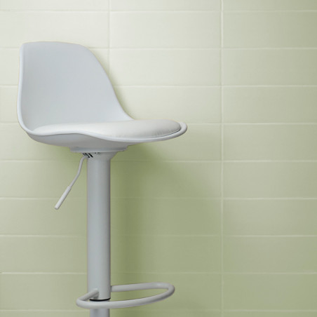 Um banco de bar giratório branco fica encostado em uma parede de azulejos verdes claros, com sua alavanca visível, evocando um a Um banco de bar giratório branco fica encostado em uma parede de azulejos verdes claros, com sua alavanca visível, evocando um a