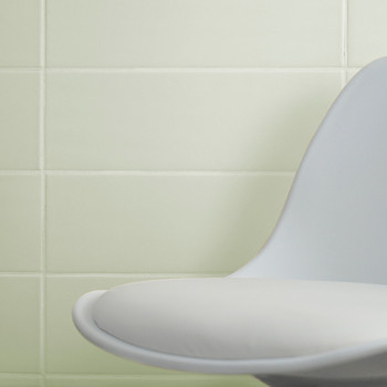 Uma moderna cadeira branca curva fica encostada em uma parede de azulejos verdes claros e lisos, criando um ambiente interior mi