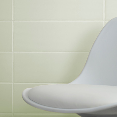 Een moderne, gebogen witte stoel staat tegen een muur van gladde, lichtgroene tegels, waardoor een minimalistische interieuromge Een moderne, gebogen witte stoel staat tegen een muur van gladde, lichtgroene tegels, waardoor een minimalistische interieuromge