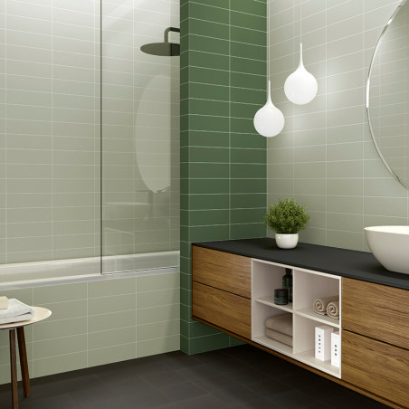 Badezimmer mit hell- und dunkelgrünen Fliesen. Badewanne mit Glasscheibe. Holzwaschtisch mit einem Waschbecken, einer Pflanze un