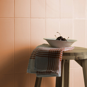 Un tabouret en bois contient un bol blanc avec des cerises et un tissu à carreaux rouges sur un fond de carreaux couleur pêche.