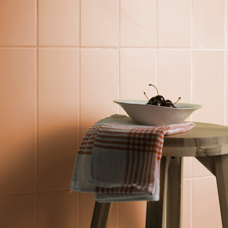Un tabouret en bois contient un bol blanc avec des cerises et un tissu à carreaux rouges sur un fond de carreaux couleur pêche.