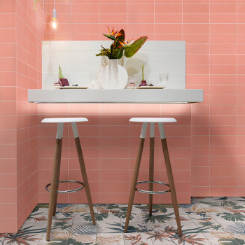 Deux tabourets en bois se dressent sur un comptoir blanc orné d'un vase de fleurs, contre des murs carrelés de roses et des carr