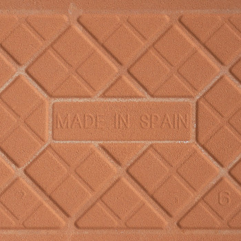 Een terracotta tegel is voorzien van de tekst `MADE IN SPAIN` in reliëf, omgeven door een geometrisch patroon van elkaar kruisen