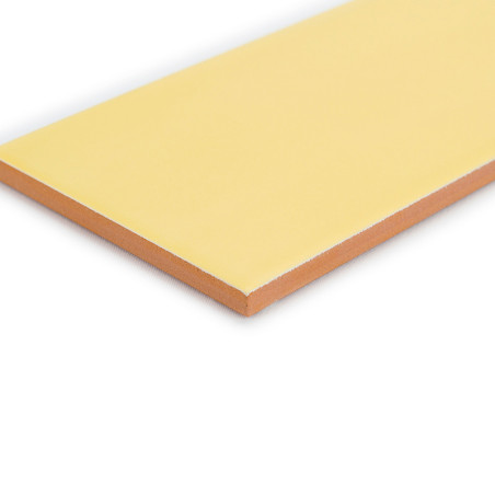 Un carreau rectangulaire jaune pâle repose sur une surface blanche, présentant une couche supérieure lisse avec un bord brun ora