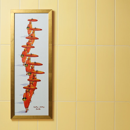 Une œuvre d’art encadrée représente une colonne de personnages vêtus de robes orange, tenant des parapluies rouges, contre un mu