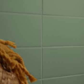 Una cuadrícula de azulejos rectangulares verdes forma una pared lisa, parcialmente oscurecida por la textura desenfocada de fibr