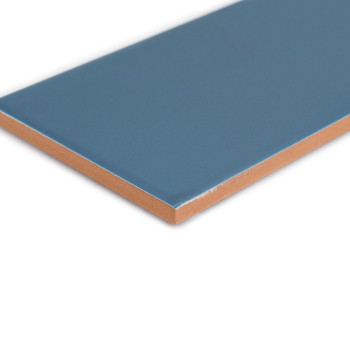 Un carreau de céramique rectangulaire bleu repose à plat sur un fond blanc, montrant sa surface lisse et son bord marron contras