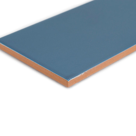 Un azulejo cerámico azul rectangular se encuentra plana sobre un fondo blanco, mostrando su superficie lisa y su borde marrón co