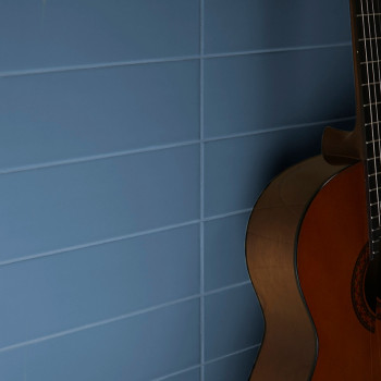 Um violão está encostado em uma parede composta por azulejos horizontais azuis, com as cordas do violão levemente visíveis e nen