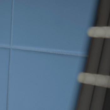 Blaue Keramikfliesen bilden ein Gittermuster an einer Wand, auf der rechten Seite ist teilweise ein Metallrohr sichtbar.