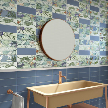 Um espelho redondo está montado em uma parede com azulejos azuis e seções com padrões tropicais. Abaixo, uma pia bege com tornei