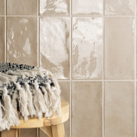 Glänzende beige Fliesen reflektieren das Licht und erzeugen eine glänzende Oberfläche. Ein runder Holzhocker mit fransigem schwa