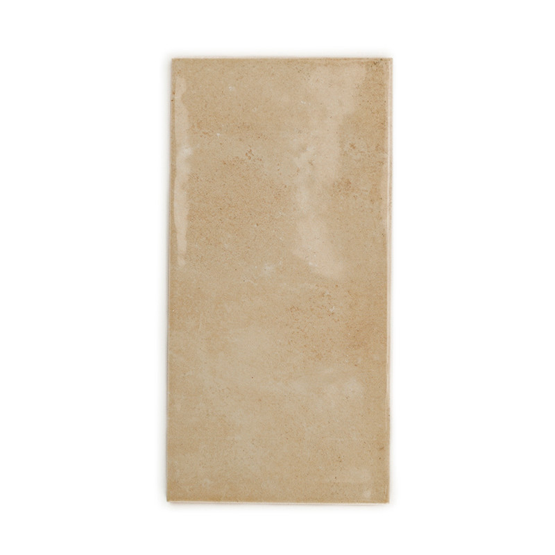 Un azulejo beige rectangular con un acabado liso y brillante se encuentra sobre un fondo blanco liso.