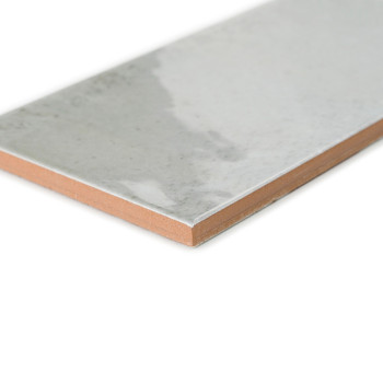 Un azulejo cerámico rectangular presenta una superficie gris lisa y brillante con un borde de color terracota, que descansa sobr