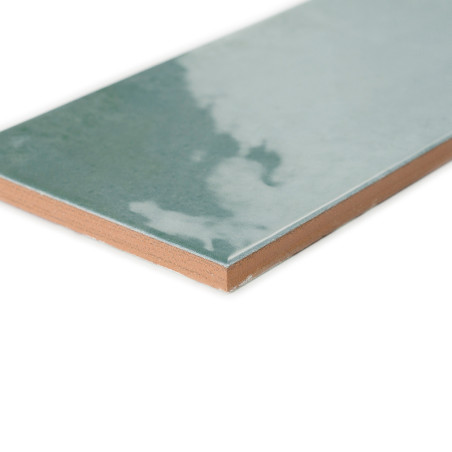 Un carreau de céramique rectangulaire, présentant une surface bleu-vert brillante avec un motif nuageux, repose sur un bord marr