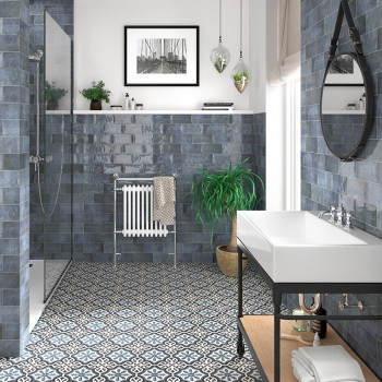 De wastafel met strak design staat in een badkamer met vloertegels met patronen, blauwe wandtegels en decoratieve planten.
