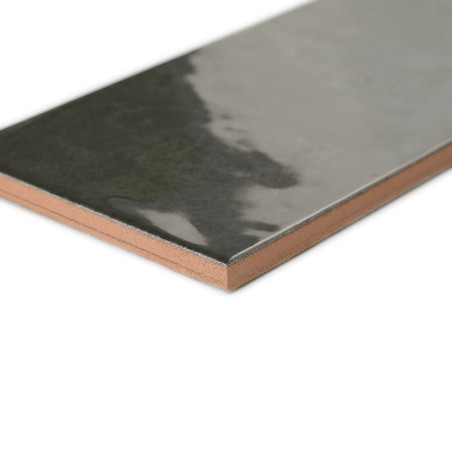 Un carreau de céramique rectangulaire et brillant s'étend en diagonale et reflète la lumière sur sa surface sombre. La tuile est