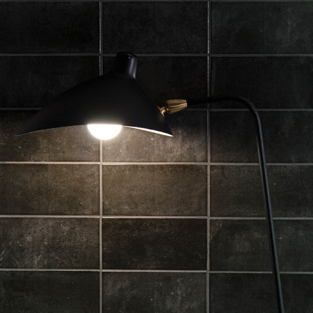 Une lampe noire illumine les murs carrelés sombres et brillants. La lumière crée un contraste avec les carreaux, mettant en vale