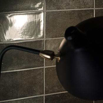 Eine mattschwarze Lampe erstreckt sich über eine glänzende, reflektierende Fliesenwand und erzeugt einen Kontrast zwischen helle