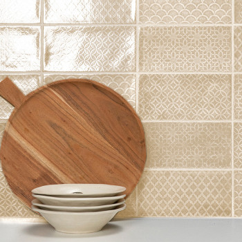 Une planche à découper en bois est appuyée contre un mur de carrelage texturé à motifs beiges, avec trois bols blancs empilés au